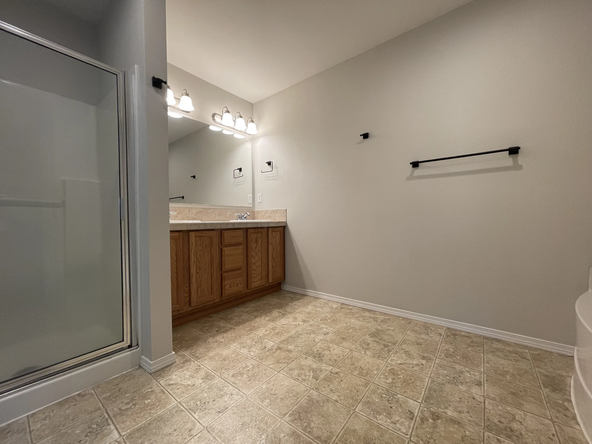 Bathroom before renovation: oak vanity with tiled counter, framed shower stall and beige vinyl floor