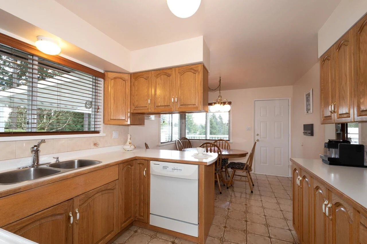 Kitchen before renovation: oak cabinets, laminate counters, white dishwasher and tiled floor