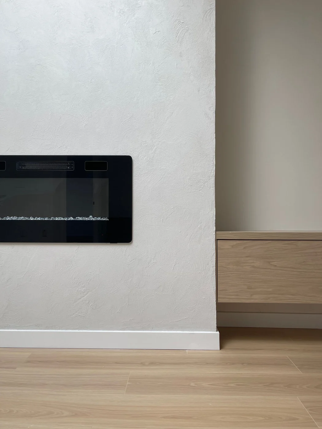 Hand-troweled plaster feature wall with a linear fireplace, beside a floating white-oak cabinet and wide-plank floor