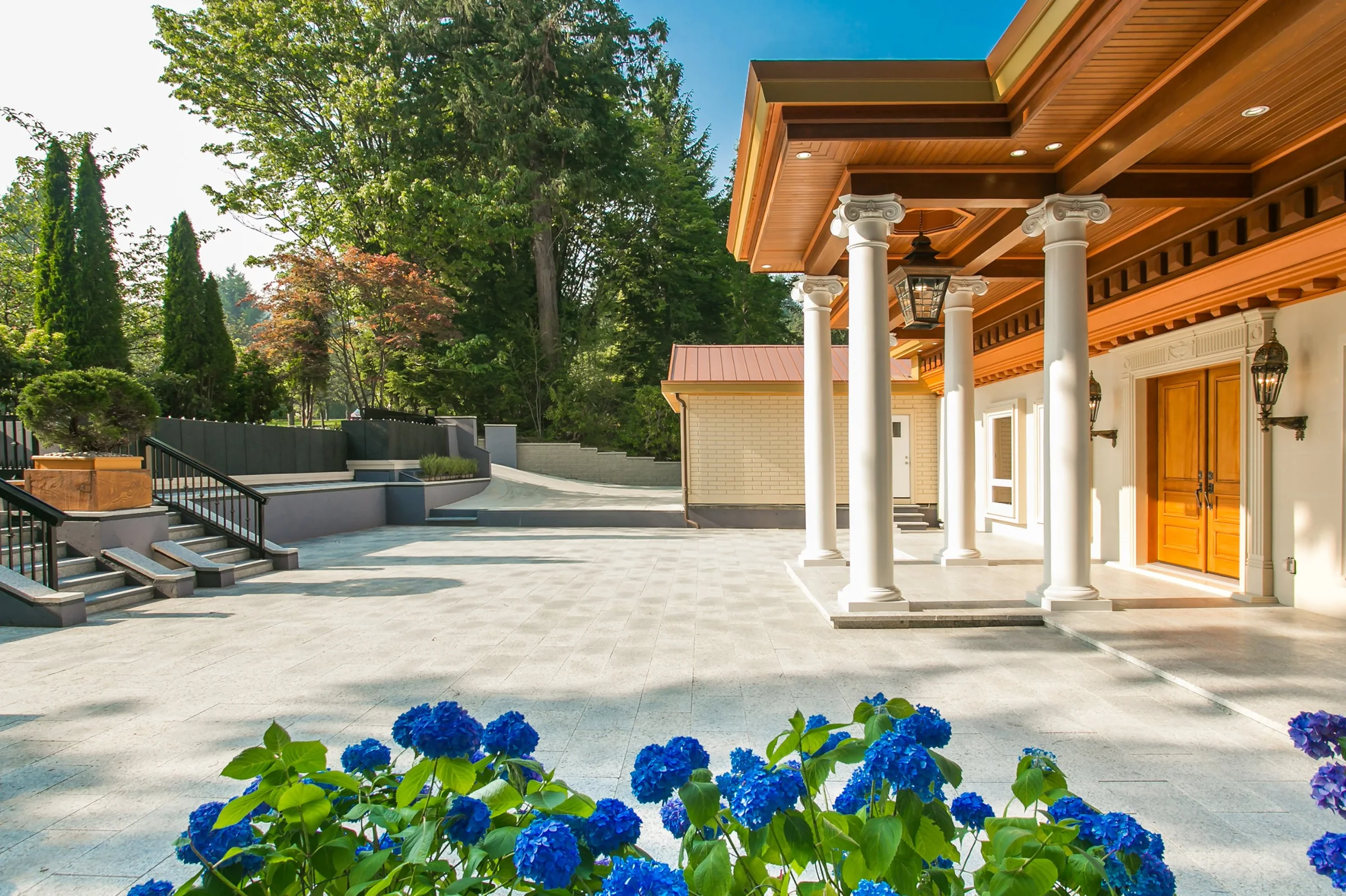 Granite courtyard and columned entry porch of a Comhome project, with blue hydrangeas in the foreground